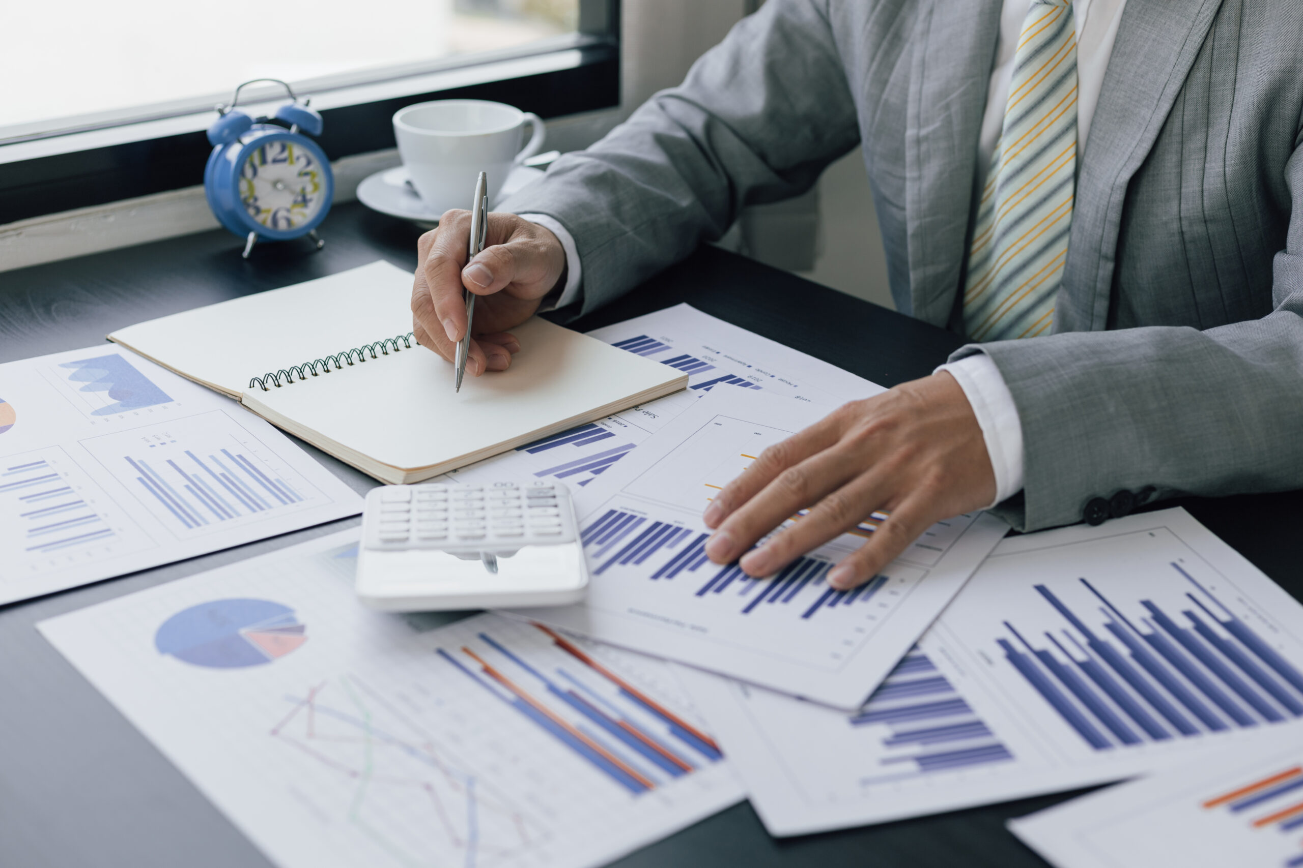 Businessman writing notes on financial reporting notepad and working using desk calculator, tax, accounting, statistics and statistical analysis concepts.